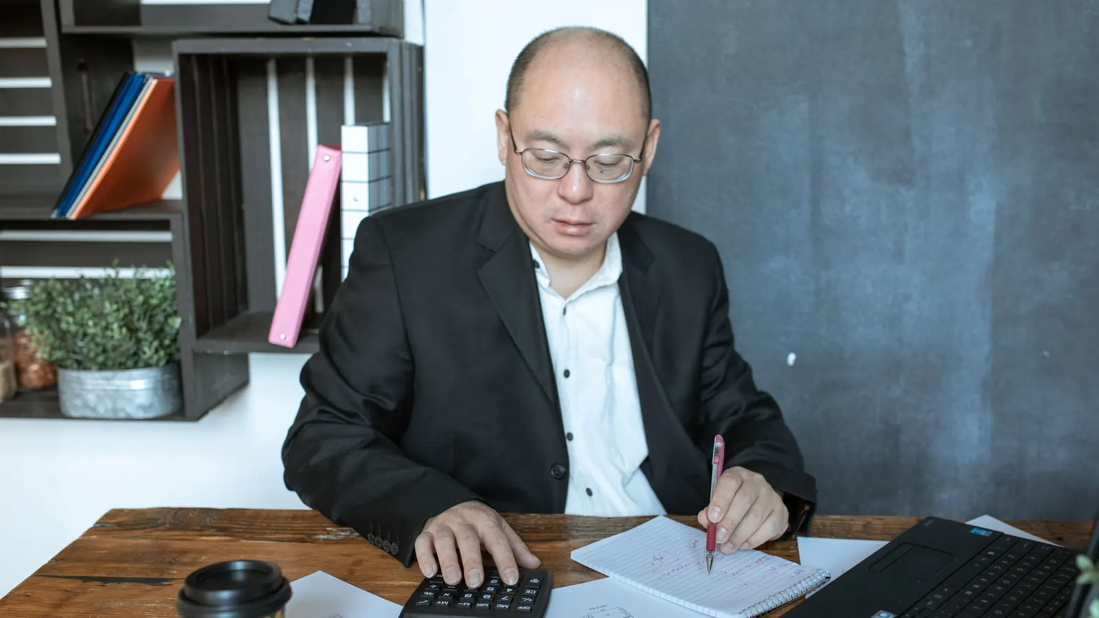 男士在辦公桌前用計算機核算並寫筆記